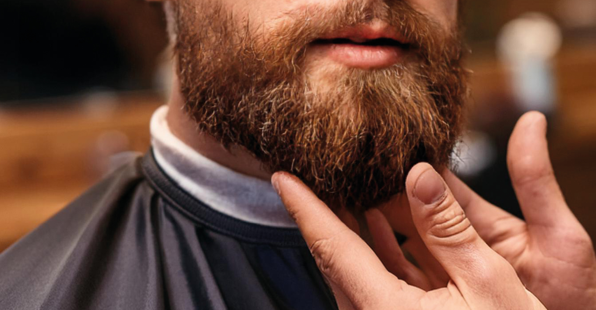 Volto di un uomo con barba lunga e delle mani di un barbiere che applica l'olio alla barba